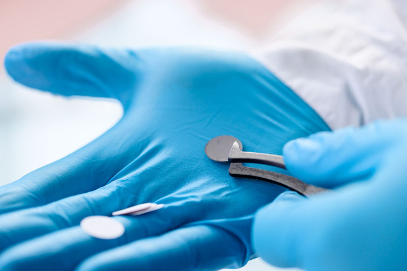 A gloved hand holds a SiBoost electrode disc with tweezers